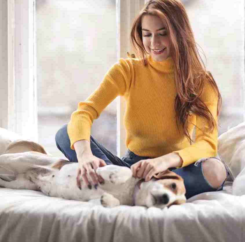 A woman pets her dog on her bed.